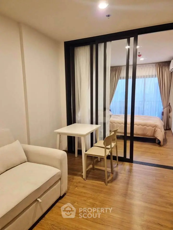 Modern studio apartment with sliding glass doors separating bedroom and living area, featuring wooden flooring.