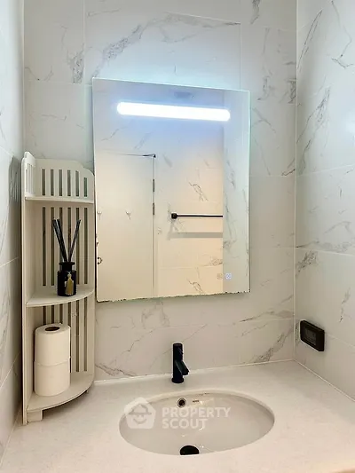 Modern bathroom with sleek vanity and illuminated mirror, featuring elegant marble tiles.