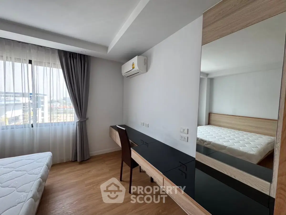 Modern bedroom with large window, wooden flooring, and sleek furniture in a bright apartment.