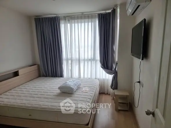 Cozy bedroom with large window and modern furnishings in a high-rise apartment.