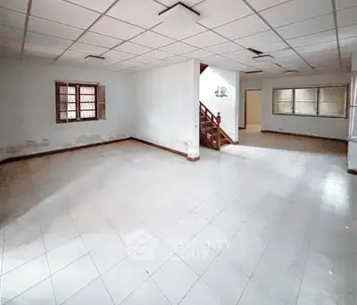 Spacious empty room with tiled flooring and staircase, ideal for customization.