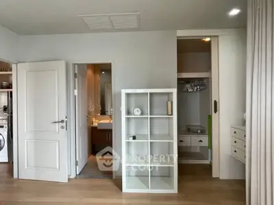 Modern interior with open closet and bathroom view, featuring sleek shelving and neutral tones.