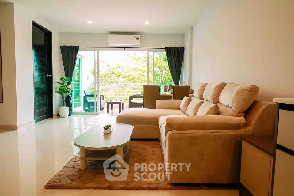 Spacious living room with modern furniture and large windows opening to a balcony with greenery view.