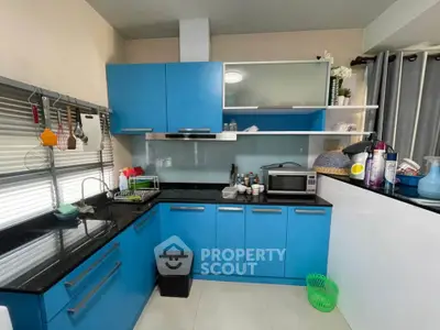 Modern kitchen with blue cabinets and black countertops, featuring a microwave and organized shelving.