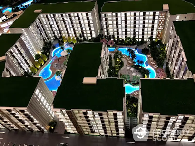 Aerial view of a luxurious residential complex at night, showcasing a stunning illuminated pool amidst modern high-rise buildings.