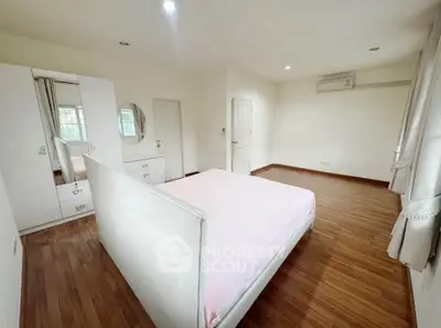 Spacious bedroom with wooden flooring and modern white furniture, featuring ample natural light.