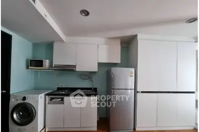 Modern kitchen with sleek white cabinets, stainless steel fridge, and washing machine in compact layout.