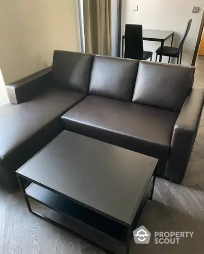 Chic modern living room with sleek dark leather sectional sofa and matching minimalist coffee table, set on elegant hardwood flooring.