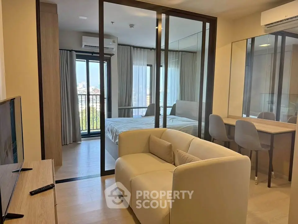 Modern apartment interior with glass-walled bedroom and cozy living area, featuring a stylish sofa and dining space.