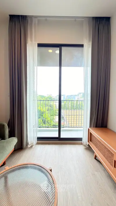 Modern living room with large window and balcony view, featuring stylish furniture and natural light.