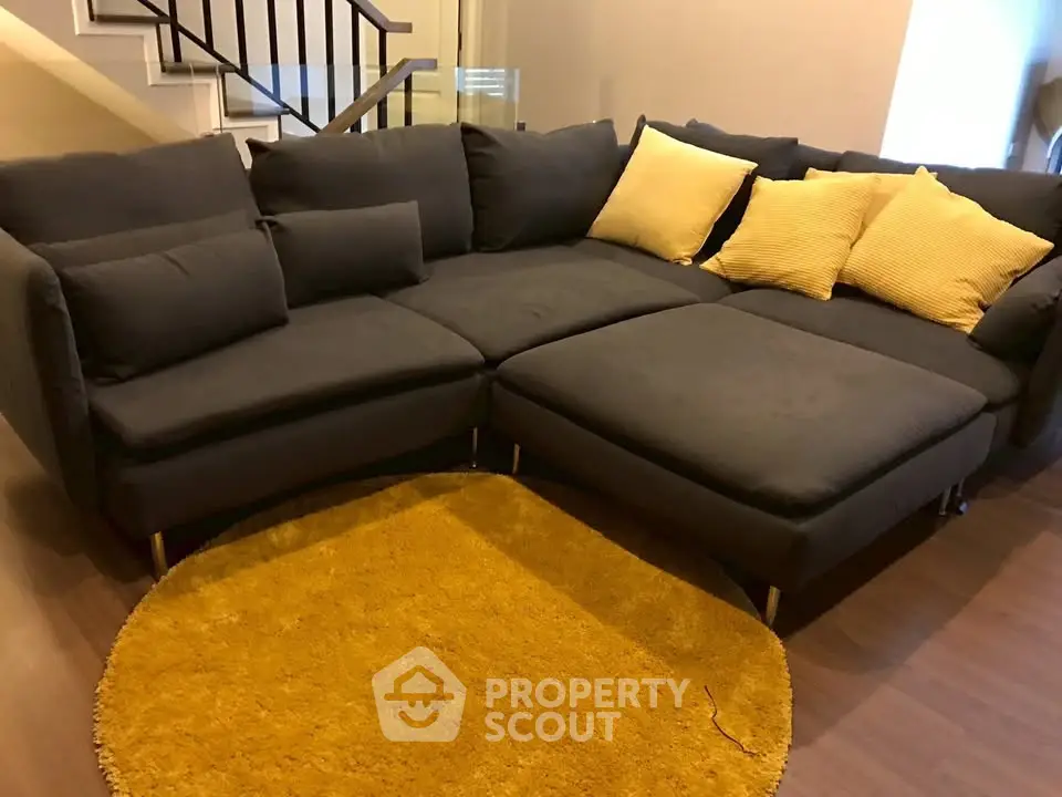 Spacious living room with modern dark sofa and vibrant yellow rug