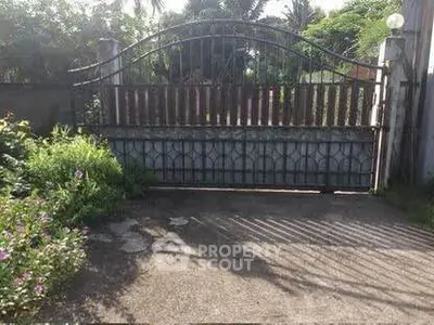 Charming gated entrance with lush greenery and paved driveway, perfect for privacy and security.