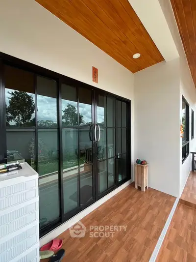 Modern balcony with wooden ceiling and sliding glass doors overlooking a lush garden view.