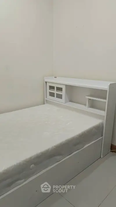 Minimalist bedroom with white bed and built-in storage headboard.