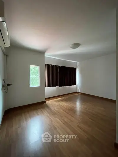 Spacious empty room with wooden flooring and large windows, perfect for customization.