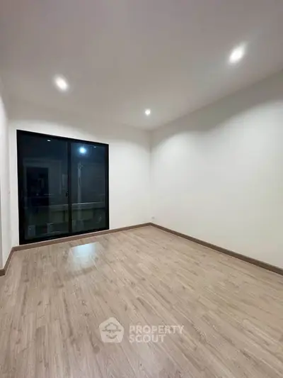 Spacious empty room with wooden flooring and large window, perfect for customization.