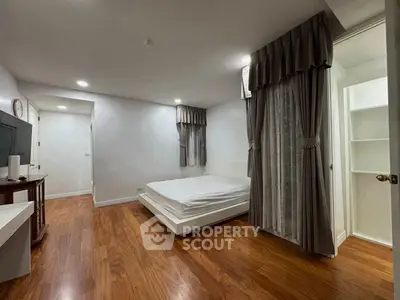 Spacious bedroom with wooden flooring and elegant curtains in modern apartment.