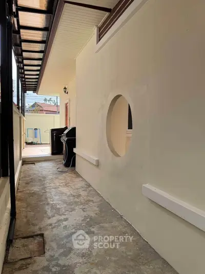 Charming exterior corridor with unique circular window and rustic flooring, perfect for creative outdoor design.