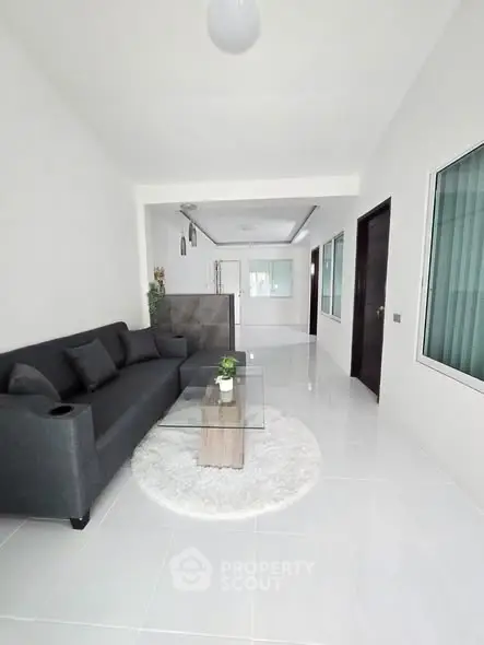 Modern living room with sleek gray sofa and glass coffee table on white tile floor.