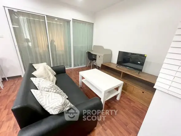 Modern living room with sleek black sofa and TV, featuring wooden flooring and large windows.