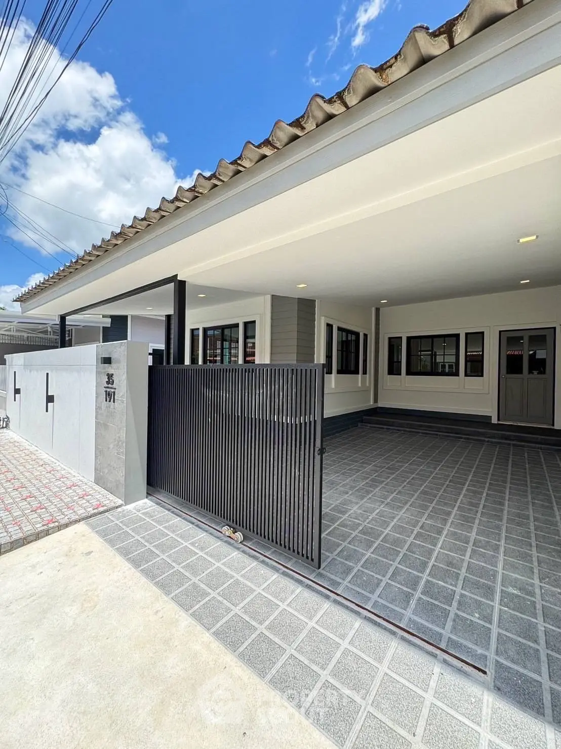 Modern single-story house with spacious driveway and sleek gate under a clear blue sky.