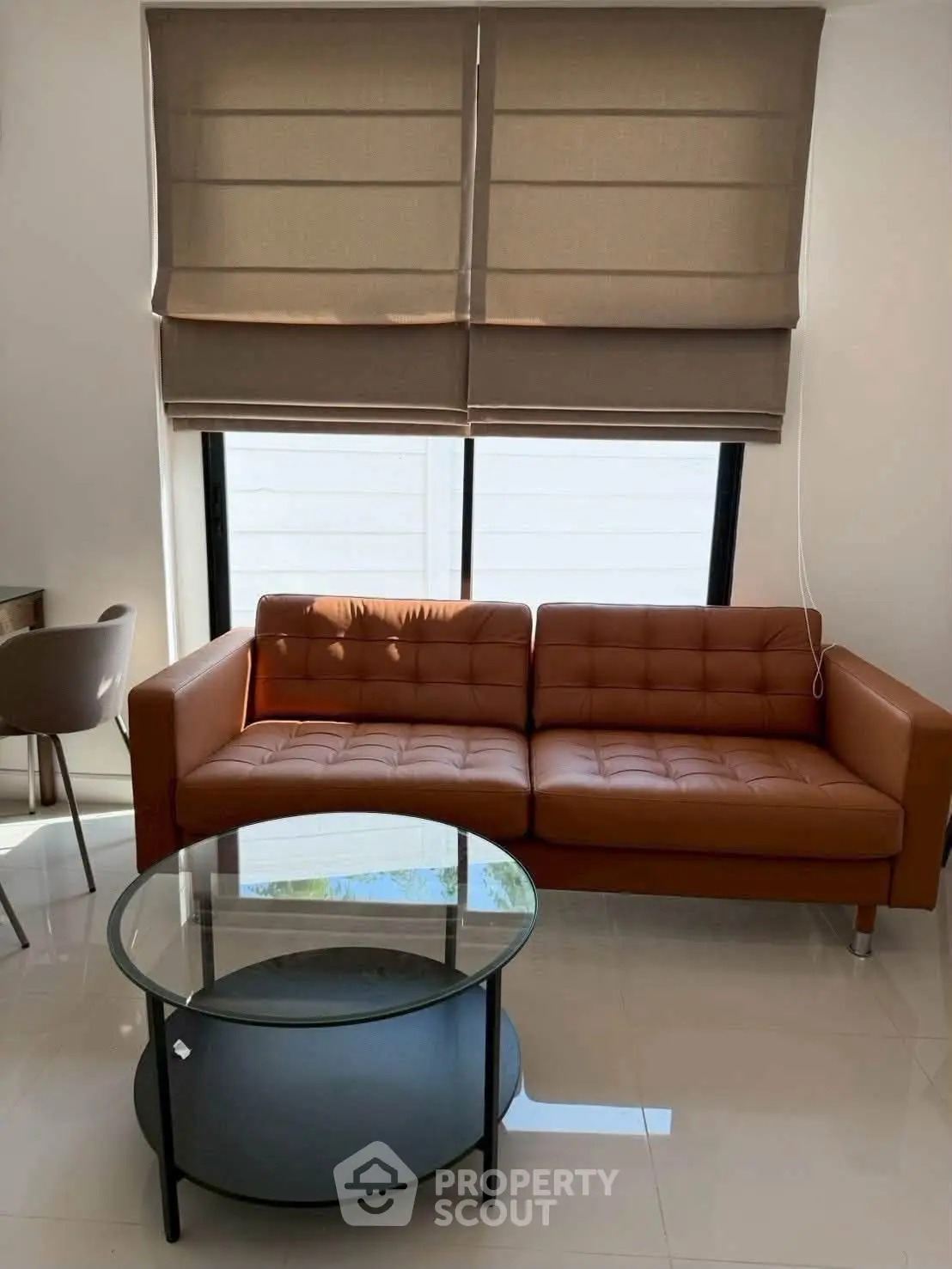 Modern living room with stylish brown sofa and glass coffee table, featuring elegant window blinds.