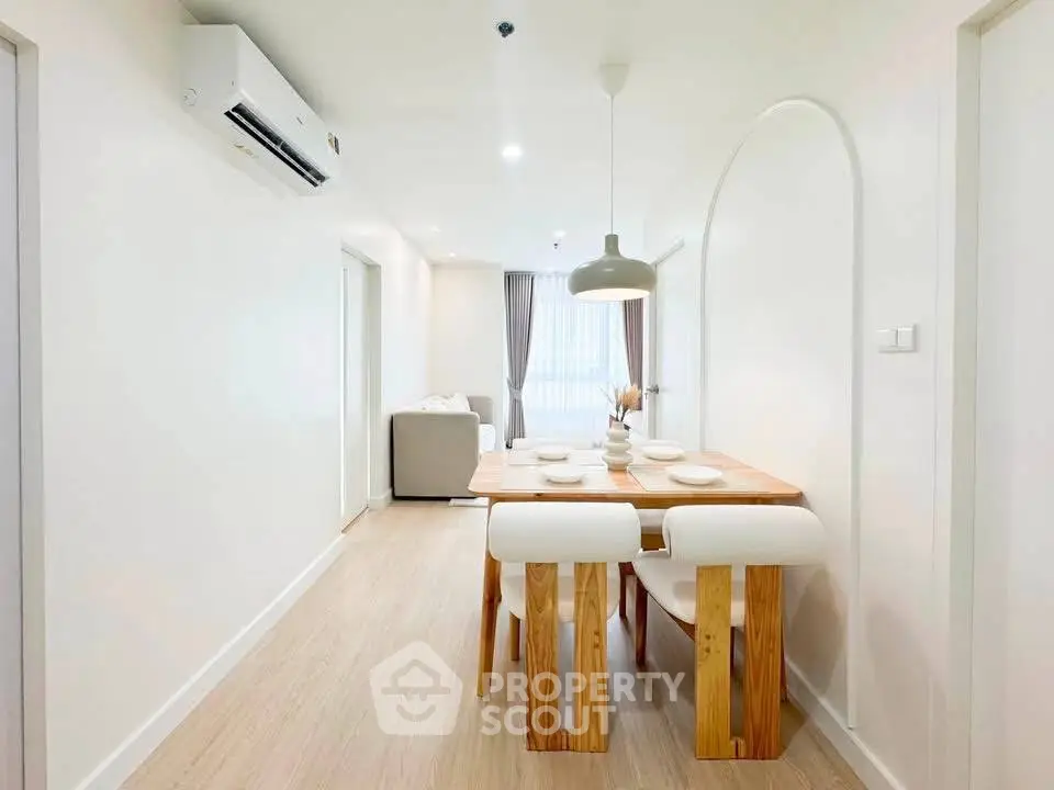 Modern dining area with wooden table and white chairs in a bright, minimalist apartment.
