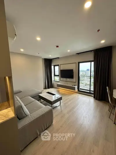 Spacious modern living room with large windows and city view, featuring sleek furniture and ambient lighting.