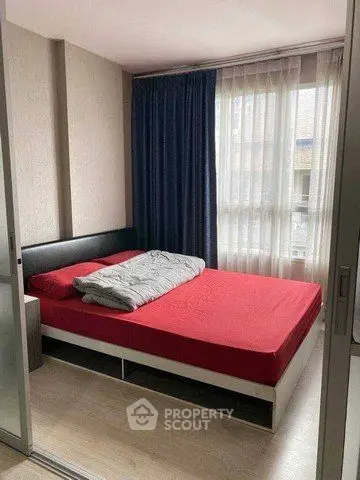 Modern bedroom with red bedding and large window, featuring sleek design and ample natural light.