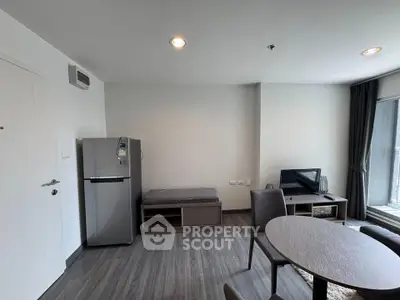 Modern living room with sleek furniture and natural light, featuring a compact fridge and TV setup.