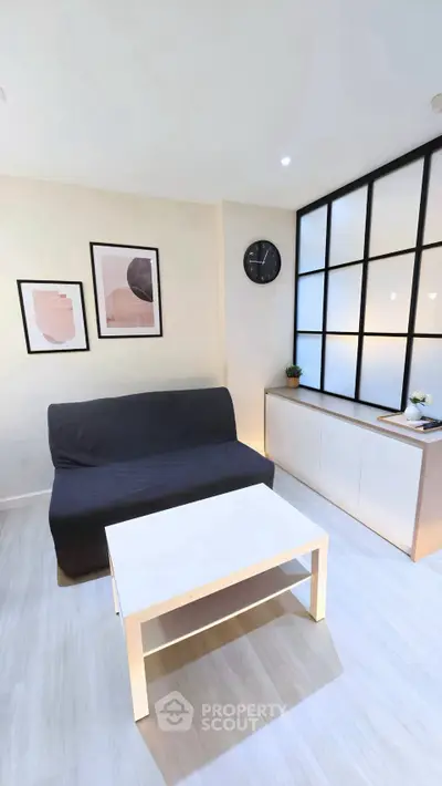 Modern living room with minimalist decor, featuring a sleek black sofa, stylish artwork, and a contemporary clock.