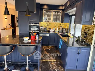 Luxurious modern kitchen with navy cabinets and gold backsplash, featuring a sleek island and high-end appliances.