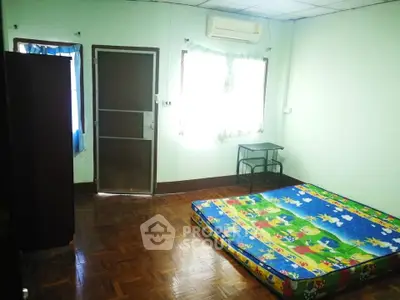 Spacious bedroom with colorful mattress and natural light, featuring wooden flooring and air conditioning.