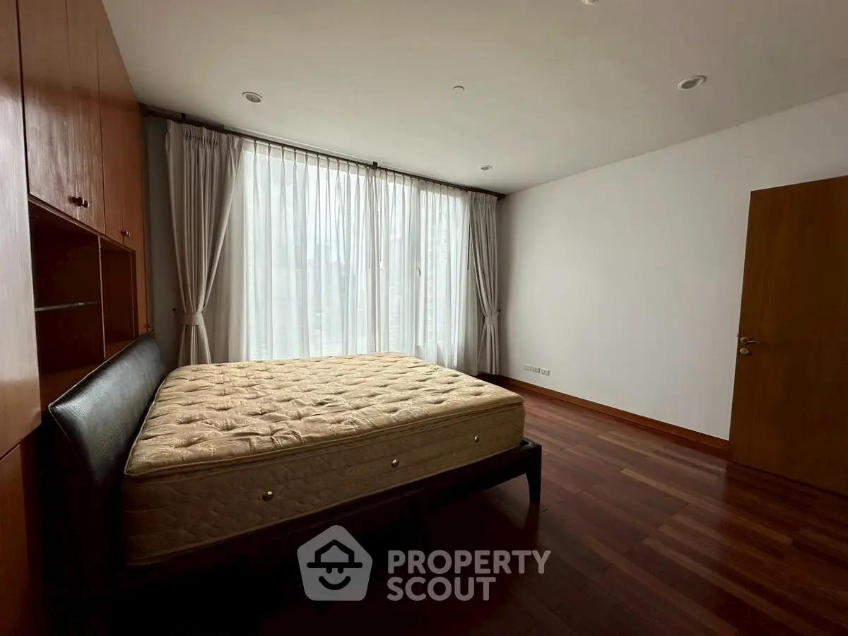 Spacious bedroom with large window and wooden flooring in modern apartment.