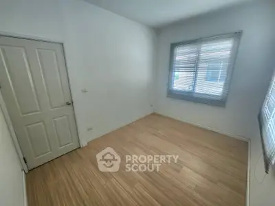 Spacious empty room with wooden flooring and large windows, perfect for customization.