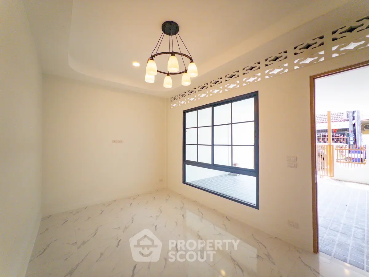 Elegant room with modern chandelier and marble flooring, featuring large window for natural light.