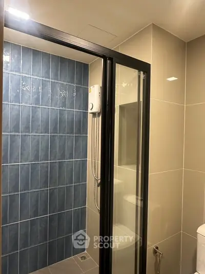 Modern bathroom with glass shower enclosure and blue tile accent wall.