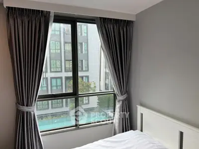 Cozy bedroom with large window offering a view of modern building and pool.