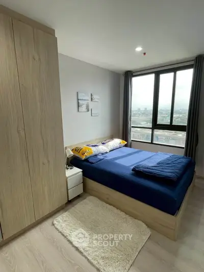 Modern bedroom with large window and city view, featuring cozy bed and stylish decor.