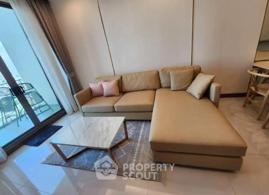 Modern living room with stylish beige sectional sofa and marble coffee table, overlooking a balcony with city view.