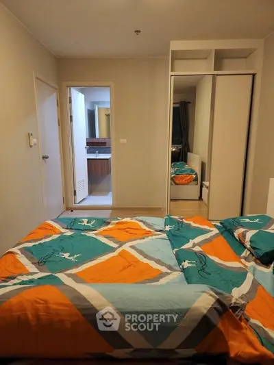 Cozy bedroom with colorful bedding and mirrored wardrobe, offering a glimpse into an adjacent bathroom.
