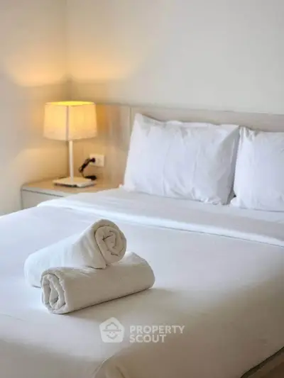 Cozy bedroom with neatly arranged white linens and soft lighting.