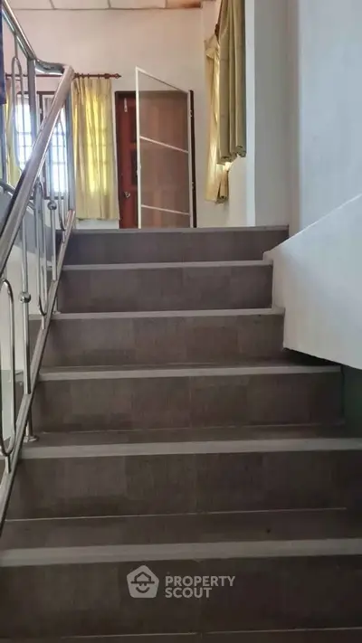 Spacious staircase with elegant railing leading to a sunlit room, ideal for modern living.