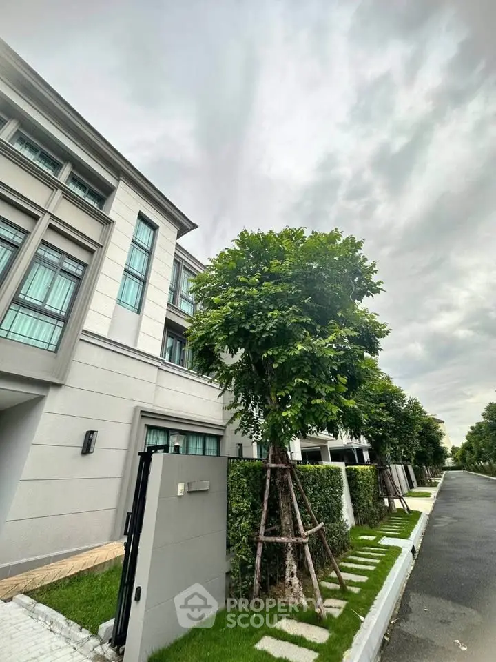 Modern townhouse exterior with lush greenery and overcast sky.