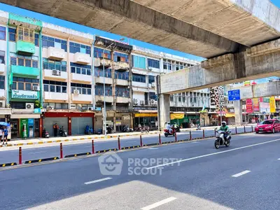 Vibrant city street view with commercial buildings and elevated train tracks.