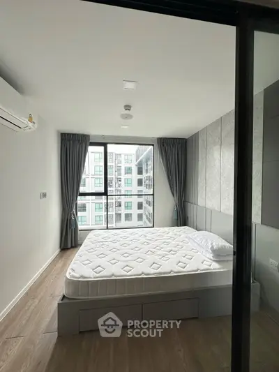 Modern bedroom with large window and city view, featuring a comfortable bed and stylish decor.