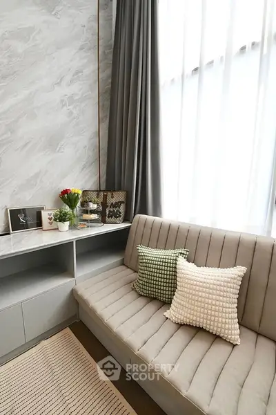 Stylish modern living room with elegant sofa and decorative pillows, featuring marble accent wall and natural light.