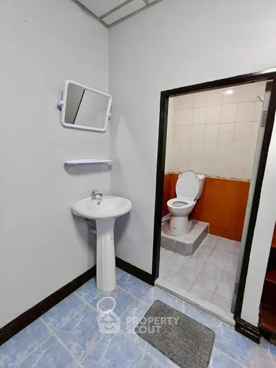 Compact bathroom with pedestal sink and elevated toilet area