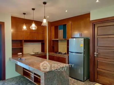 Modern kitchen with granite countertops, wooden cabinets, and stainless steel fridge in a cozy apartment.