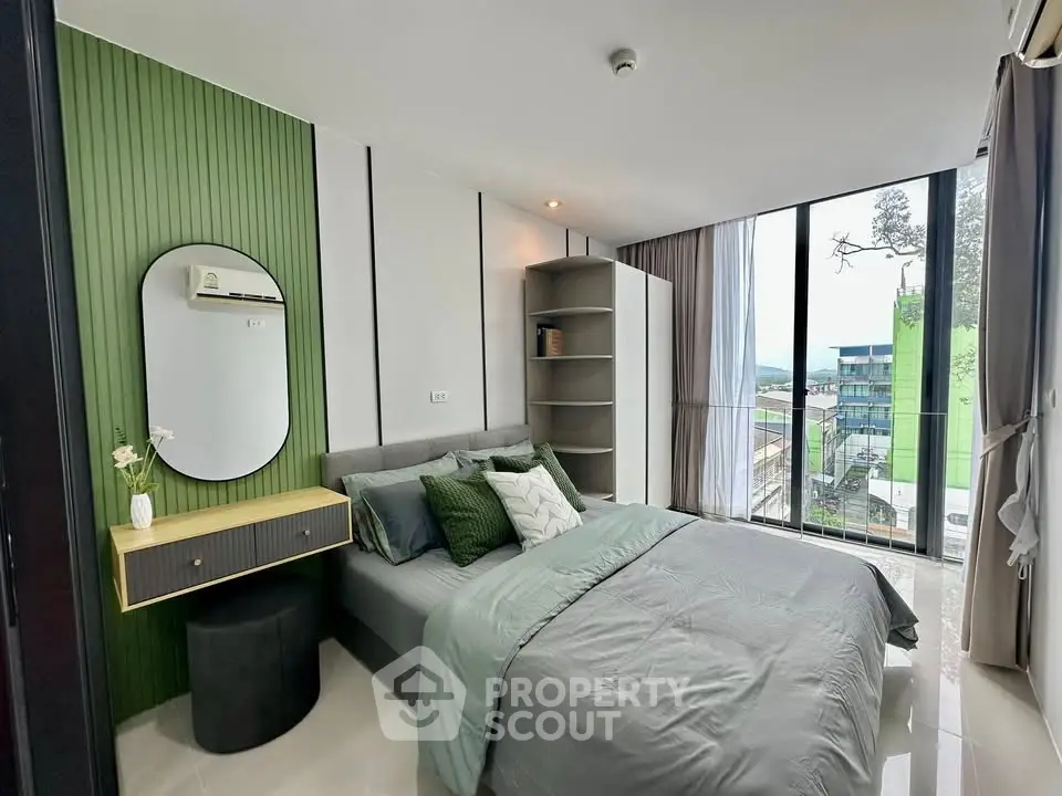 Modern bedroom with green accent wall and large windows offering city view